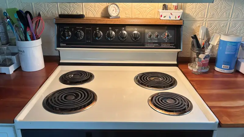 A white electric stovetop in a home kitchen with cooking utensils on wooden counters on either side.