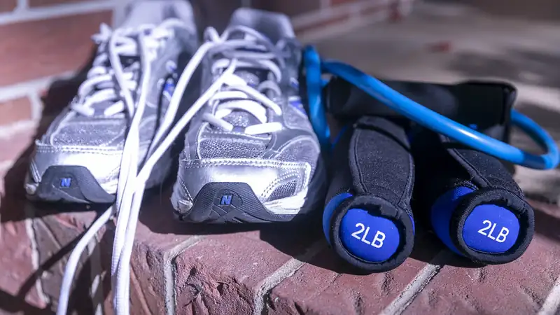 A blue resistance band, two 2 lb dumbbells and running shoes on a brick step.