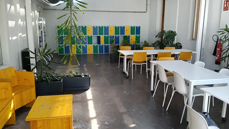 A bright office break area with white tables, yellow chairs, plants and colorful lockers.