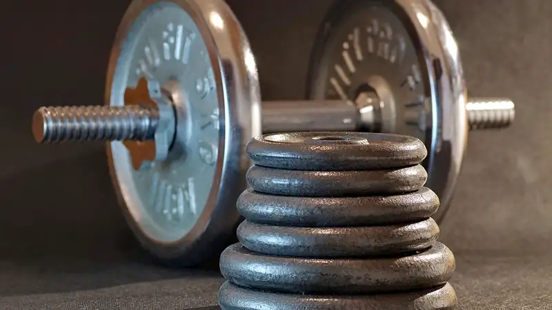 A cast-iron dumbbell resting beside a stack of round weight plates on a dark floor.