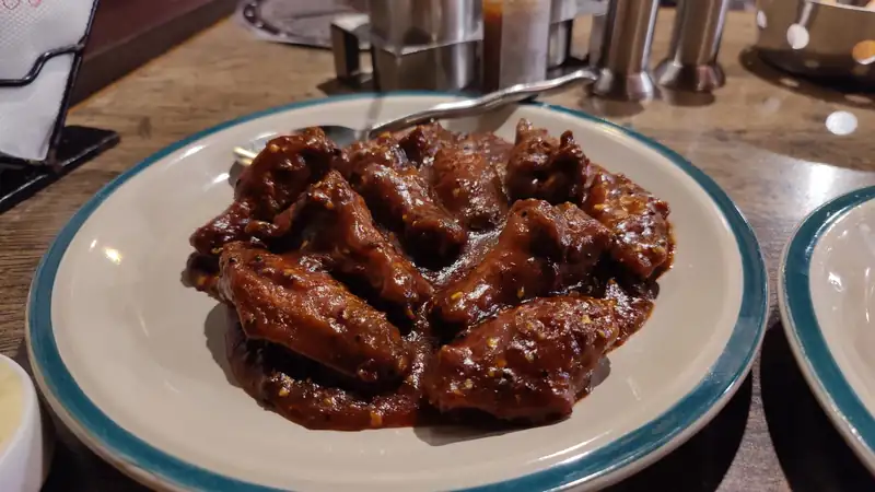 A plate of glossy barbecue chicken wings on a restaurant table.