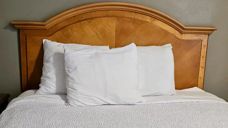 A made bed with three white pillows against a wooden headboard.