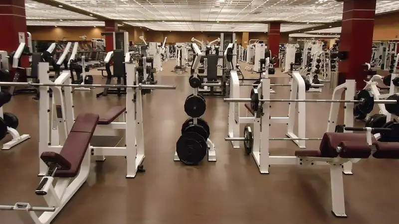 An empty commercial gym with rows of weight benches, racks and plates on a wooden floor.