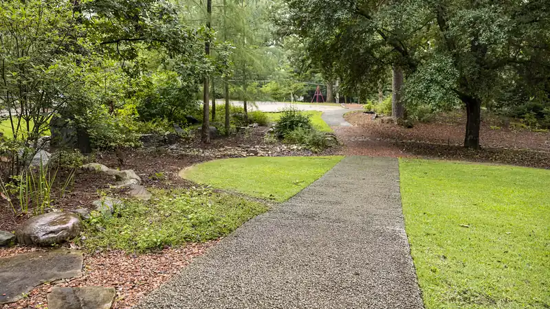 A paved walking path curving through a green public garden with trees.
