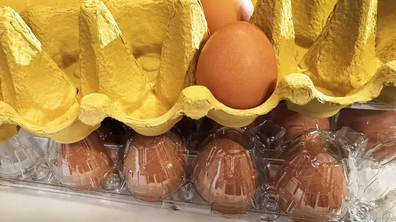 Brown eggs in a yellow pulp carton stacked on a clear plastic egg carton.
