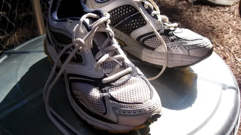 A pair of worn gray running shoes resting on a round metal lid in sunlight.