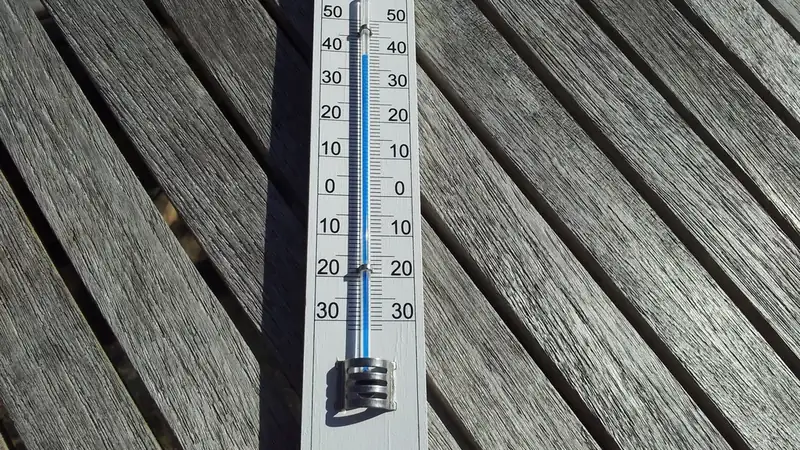 A Celsius thermometer lying on weathered gray deck boards in bright sun.