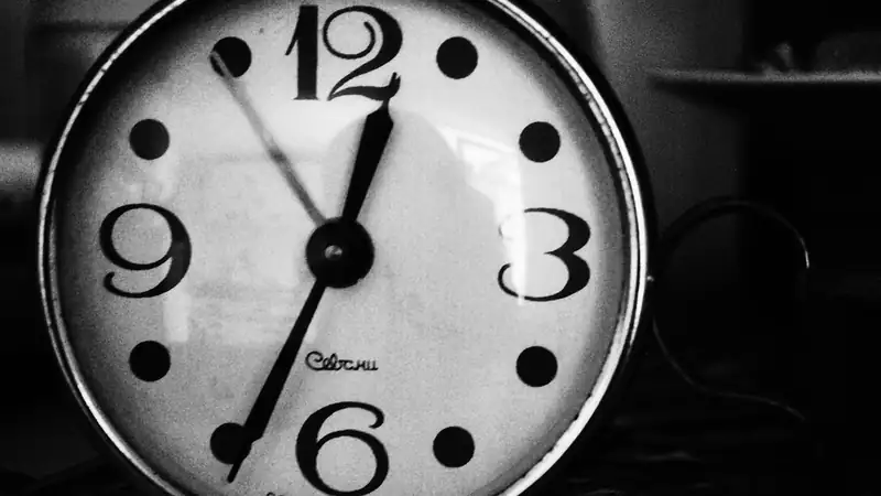 A black-and-white close-up of an alarm clock face with bold numerals.